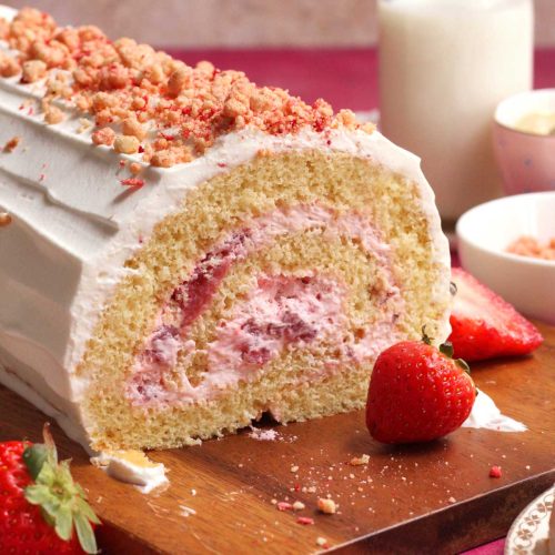 Sliced strawberry cream Swiss roll cake with fresh strawberries on a wooden board