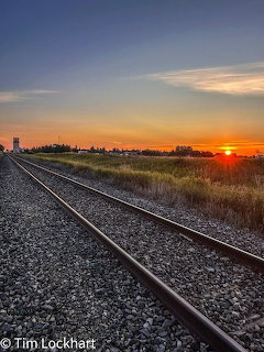 Two parallel railroad tracks extending into the distance with a colorful sunset on the right horizon