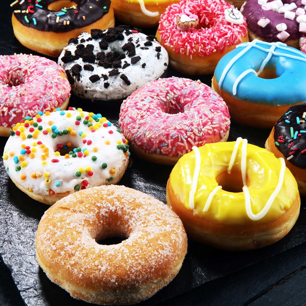 Colorful glazed donuts with various toppings and sprinkles on dark background
