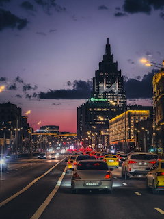City street at dusk with traffic and illuminated clock tower against twilight sky