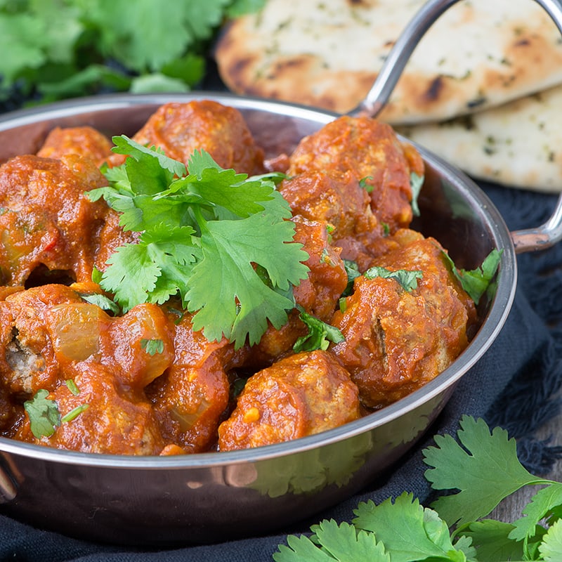 Lamb meatballs in orange curry sauce with fresh cilantro in metal bowl, naan bread alongside