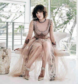 Woman in beige tulle gown seated in bright white interior