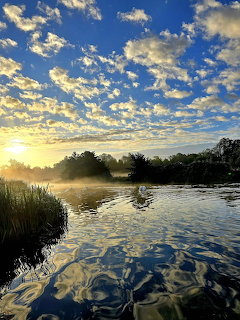 Sunrise over calm river with dramatic clouds reflected in water and misty banks