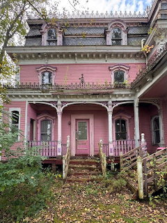 Old pink Victorian house with ornate trim, porch, and leaf-covered steps