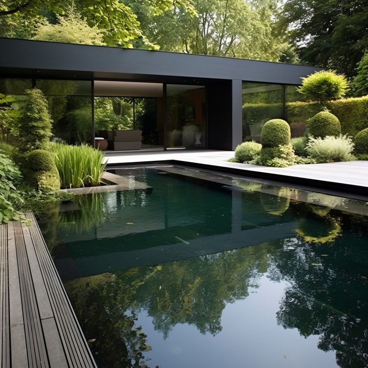 Modern glass house beside a reflective swimming pool with landscaped shrubs and trees