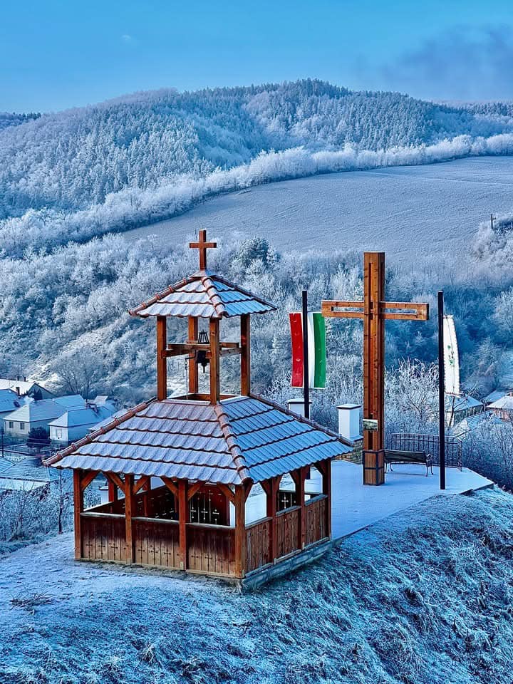 Small wooden chapel with bell tower and crosses on snow-covered hill with mountain backdrop in winter