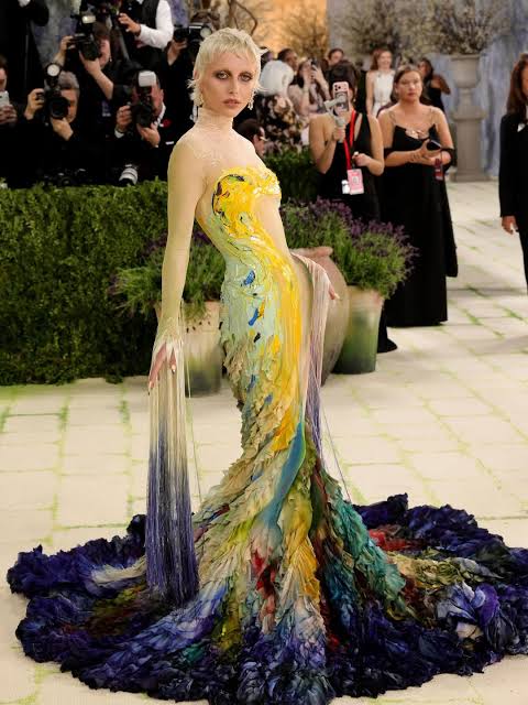 Woman in a strapless multicolor painted gown with flowing train at a formal red carpet event
