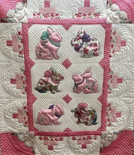 Pink and white patchwork quilt with six floral fabric rabbit appliqués arranged in a grid