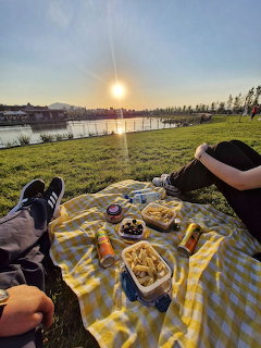 People having a picnic on a checkered blanket by a lake at sunset with mountains in the background