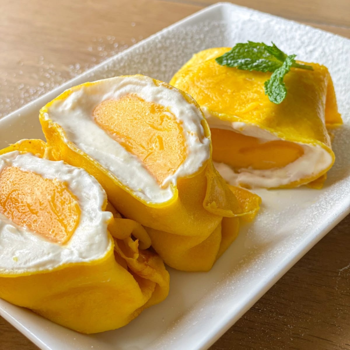 Sliced mango crepe rolls with cream filling on white plate