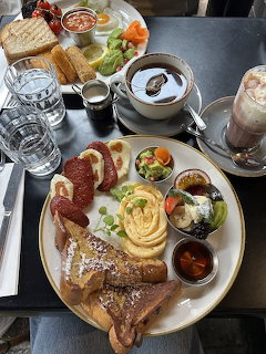 Overhead view of a full breakfast platter with various items, coffee, and a chocolate drink on a dark table