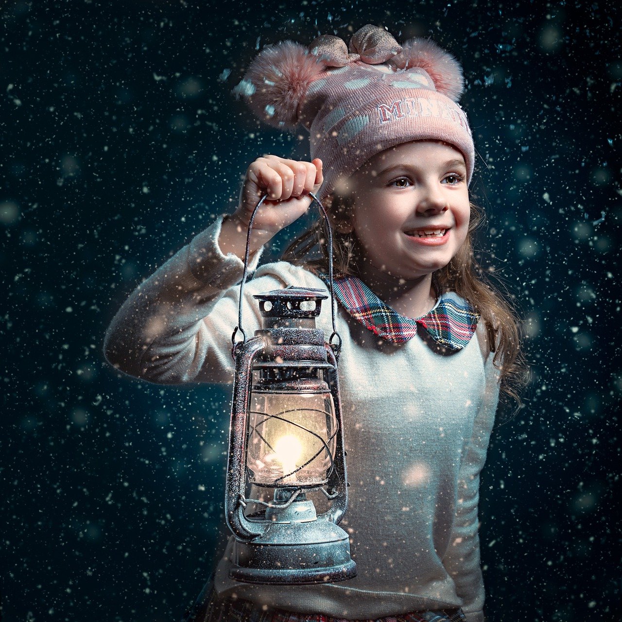 Smiling girl in pink winter hat holding glowing lantern in falling snow at night
