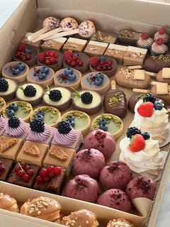 Box of assorted miniature pastries including tarts, macarons, éclairs, and cream desserts with fresh berries