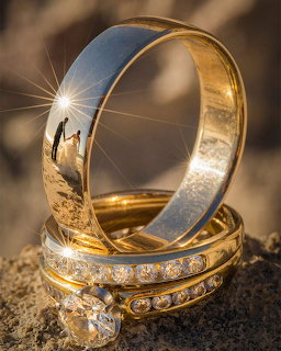 Gold wedding rings with a reflection of a couple silhouetted at sunset visible inside the larger ring