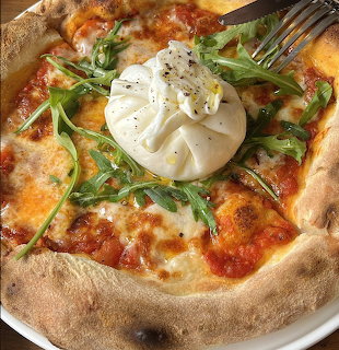 Neapolitan-style pizza topped with burata cheese, arugula, and tomato sauce on a plate