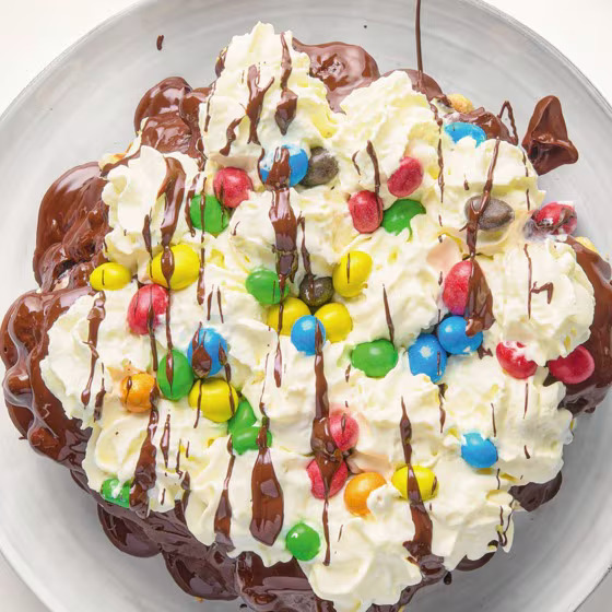 Layered wafer cake with whipped cream, chocolate sauce, and colorful M&M candies on a plate
