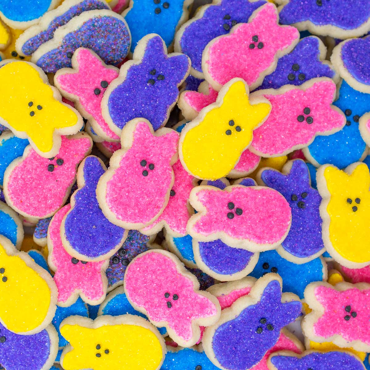 Pile of bunny and chick shaped frosted Easter cookies in bright pink, purple, yellow and blue colors