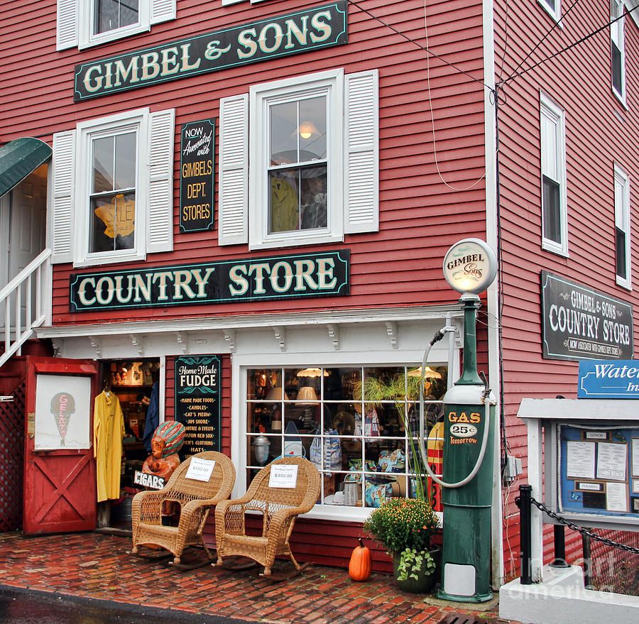 Red wooden country store building with white trim, rocking chairs on cobblestone sidewalk