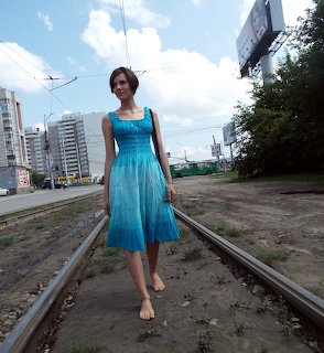 Woman in a blue dress walking barefoot on railway tracks in a city area