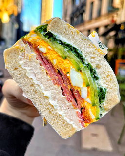Hand holding a sandwich wedge with colorful layers of egg, vegetables, and spreads on white bread