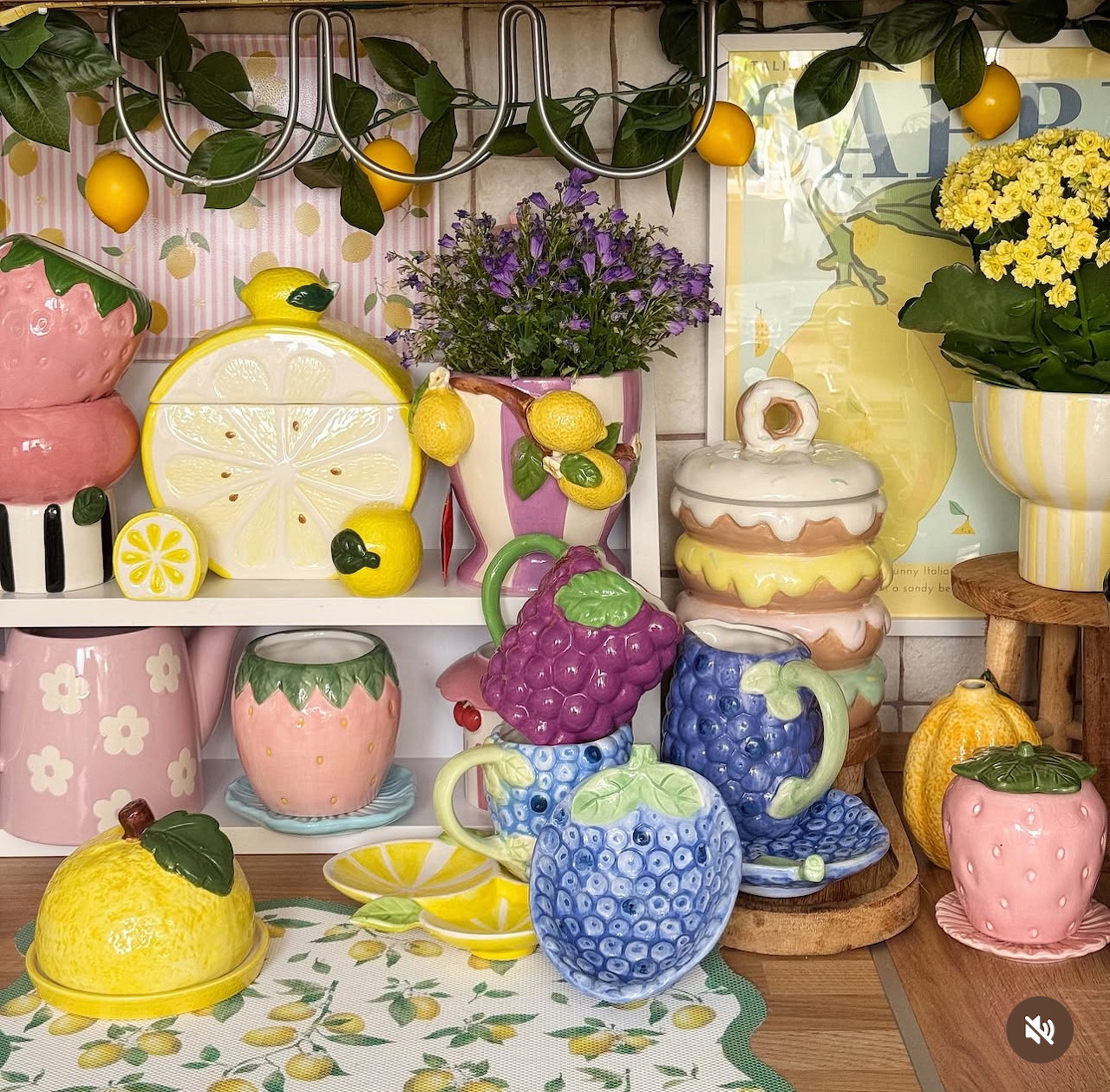 Colorful kitchen still life with lemons, floral teapots, cups, flowers, and cakes on shelves and a table