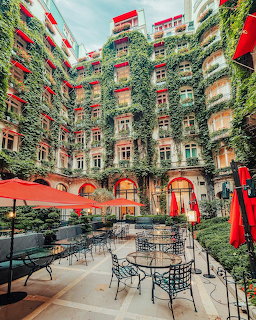 Ivy-covered courtyard of Hôtel Plaza Athénée Paris with red awnings and outdoor seating