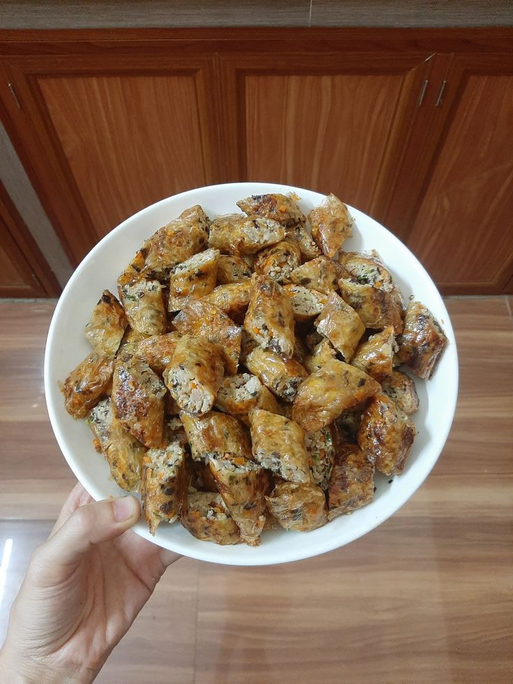 Hand holding a white plate of crispy Vietnamese eggrolls indoors