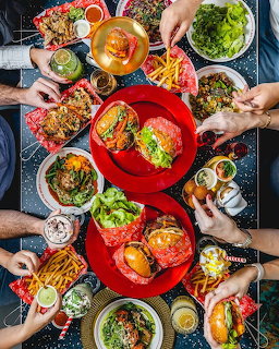Overhead flatlay of colorful brunch dishes with hands reaching for food on a dark table