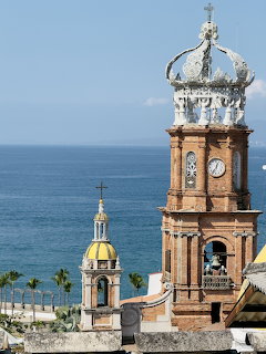 Ornate church bell tower with crown dome and clock overlooking ocean in Puerto Vallarta