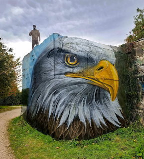 Large realistic bald eagle head mural painted on a concrete block with a person standing on top
