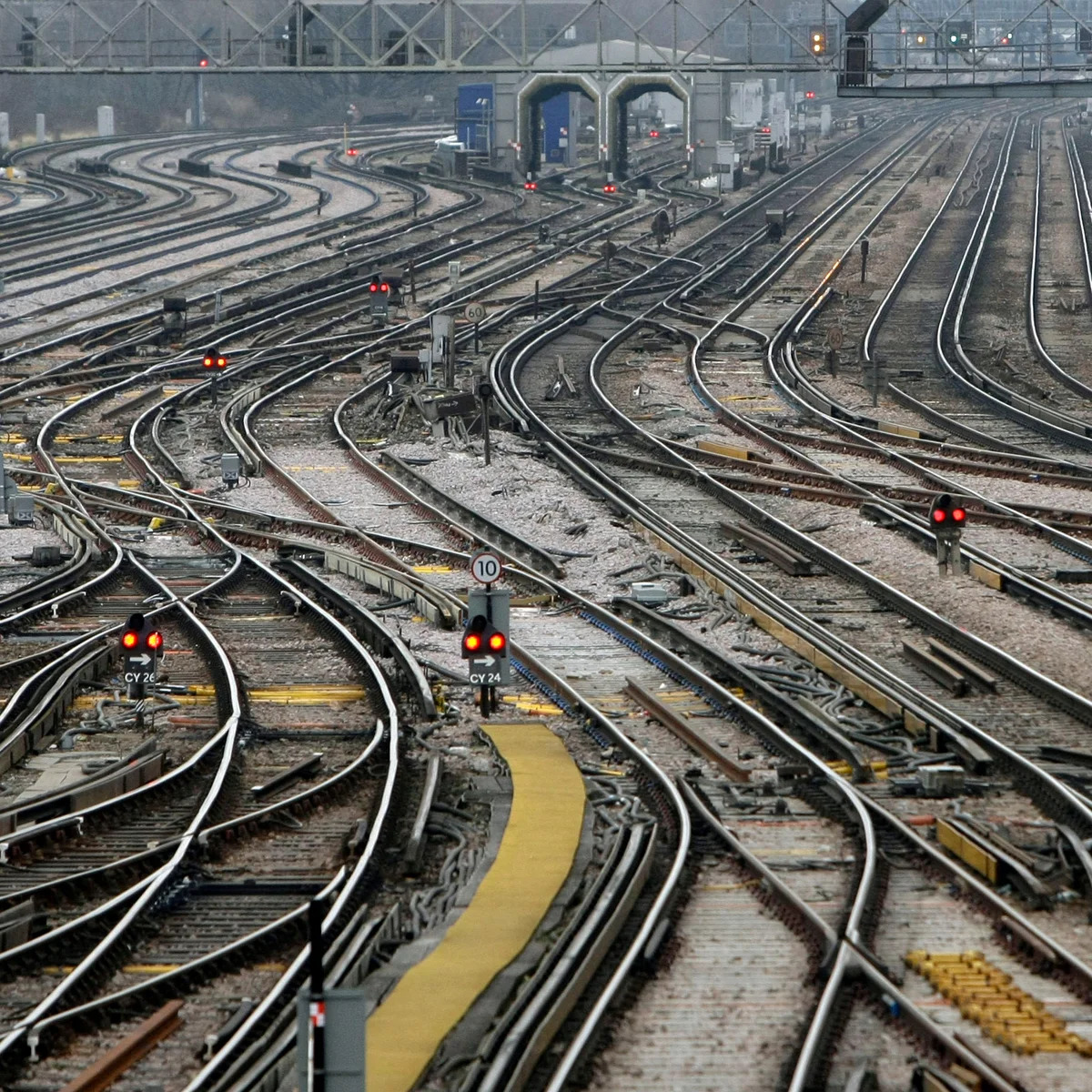 Wet railway tracks and signal lights at a busy rail junction near station platforms