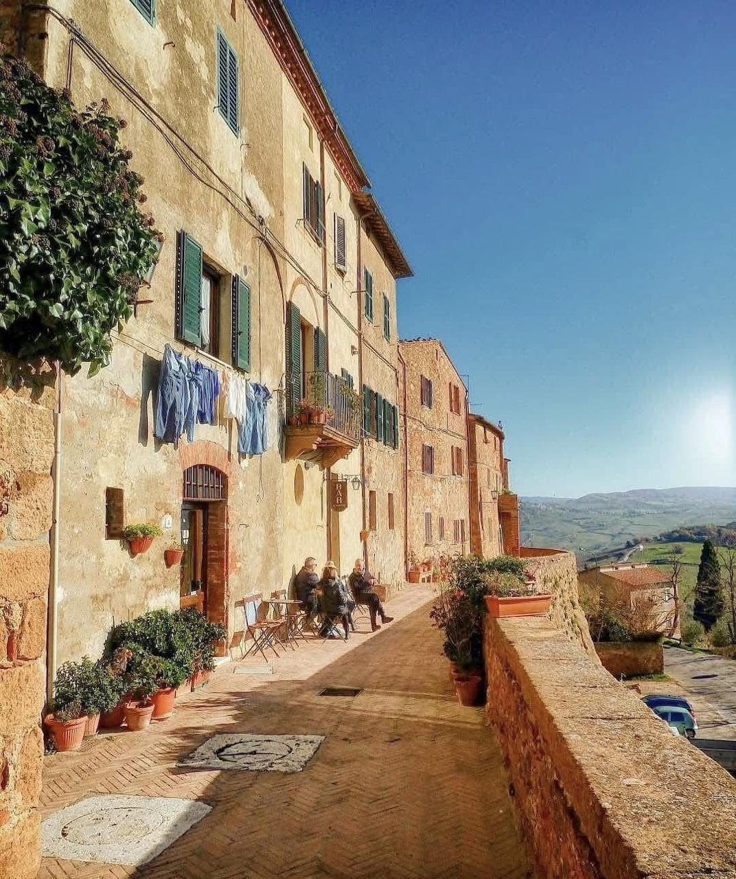 Sunny terrace in Tuscan village with stone buildings, potted plants, and countryside view