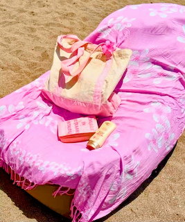 Pink floral towel on beach lounge chair with tote bag, sunscreen, and accessories on sand