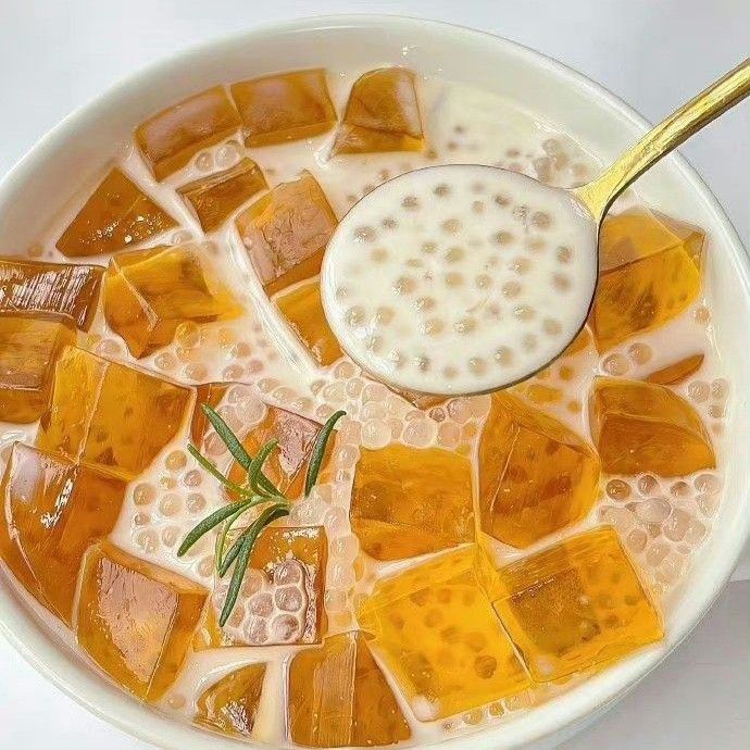 Bowl of sago dessert with milk, orange jelly cubes, and a spoon holding sago pearls