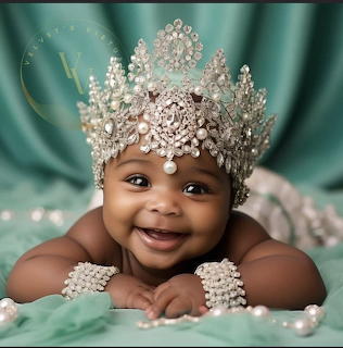 Smiling baby girl wearing ornate pearl crown and bracelets on teal fabric