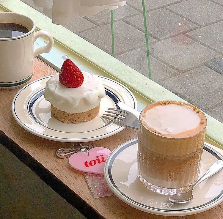 Two coffee drinks and a cream-topped dessert with a strawberry on a cafe table by a window