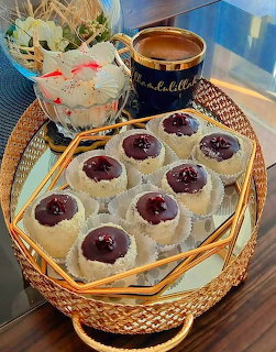 Round cookies with jam centers on woven tray next to blue coffee cup and flower pot