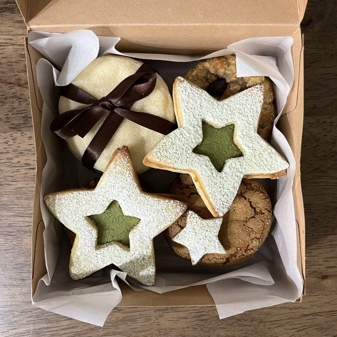 Star-shaped cookies with green centers and powdered sugar in a white box