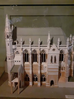 White architectural model of Victorian Gothic chapel with tall spire and ornate details in display case