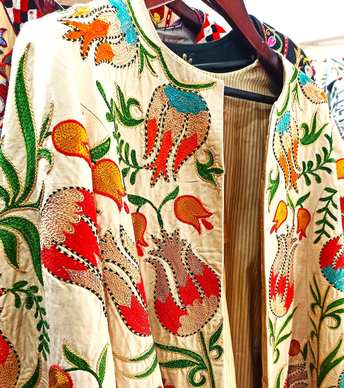 Colorful embroidered ethnic jacket with floral and bird patterns on a hanger