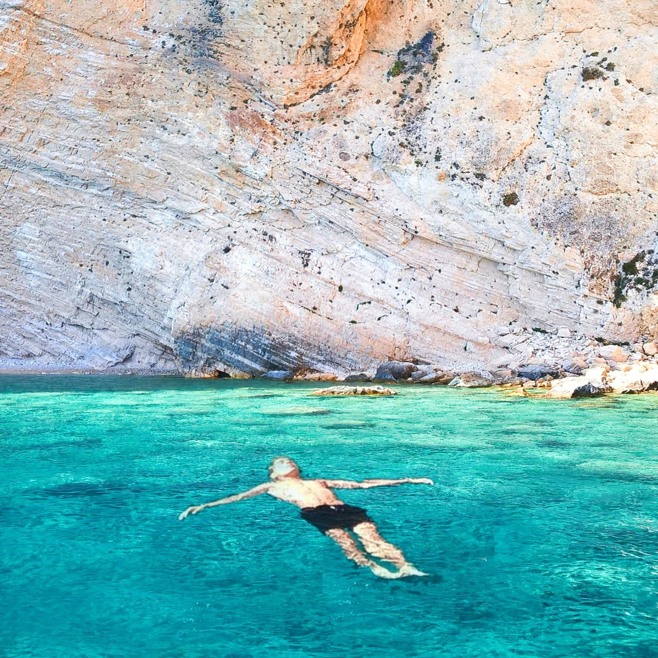 Man floating in turquoise water near a rocky cliff in Greece