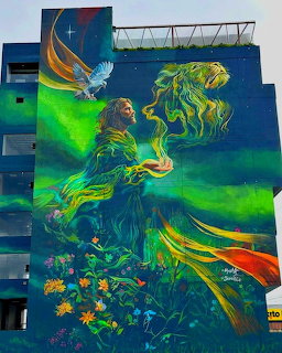 Colorful building mural of a woman in flowing green and gold robes with an owl and flowers