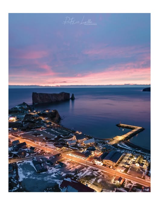 Aerial view of Percé town and Percé Rock at sunset with pink clouds and calm ocean