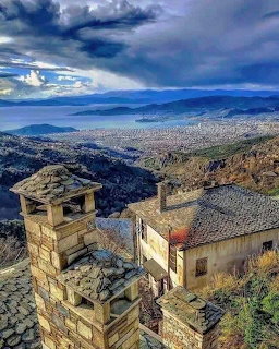 Stone bell tower and buildings on mountainside with stormy sky and sea view in Pelion, Greece