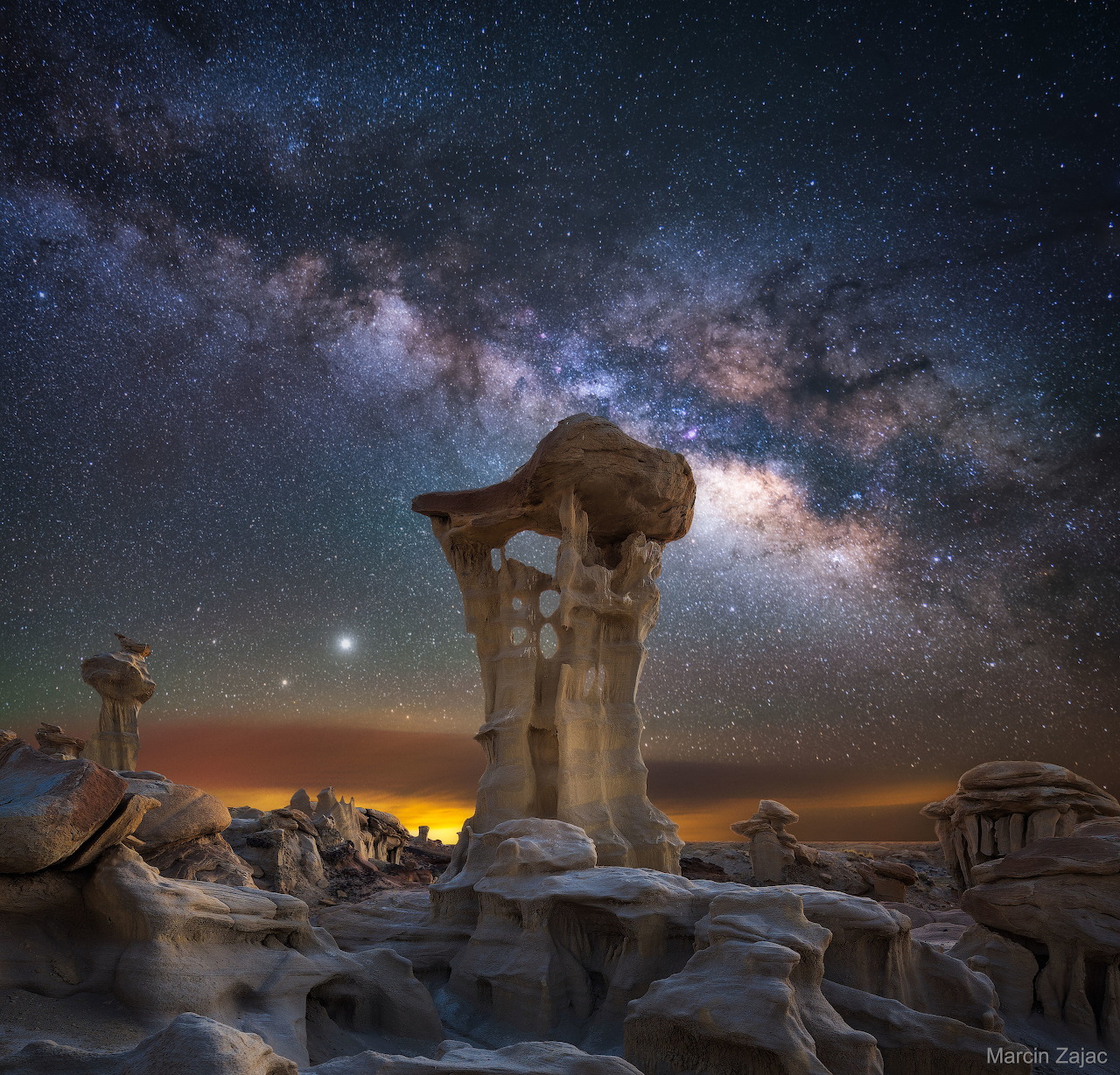 Milky Way galaxy arching over mushroom-shaped rock formation in desert at night with starry sky