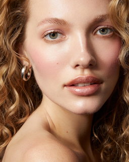 Close-up portrait of a young woman with curly blonde hair, green eyes, and gold hoop earrings