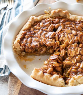 Peanut pie in white ceramic dish with one slice removed showing caramel peanut filling