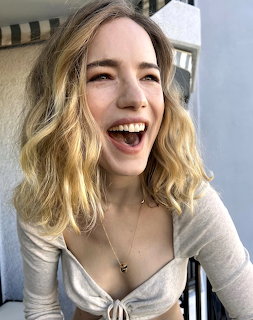 Woman with wavy blonde hair smiling broadly in light gray top