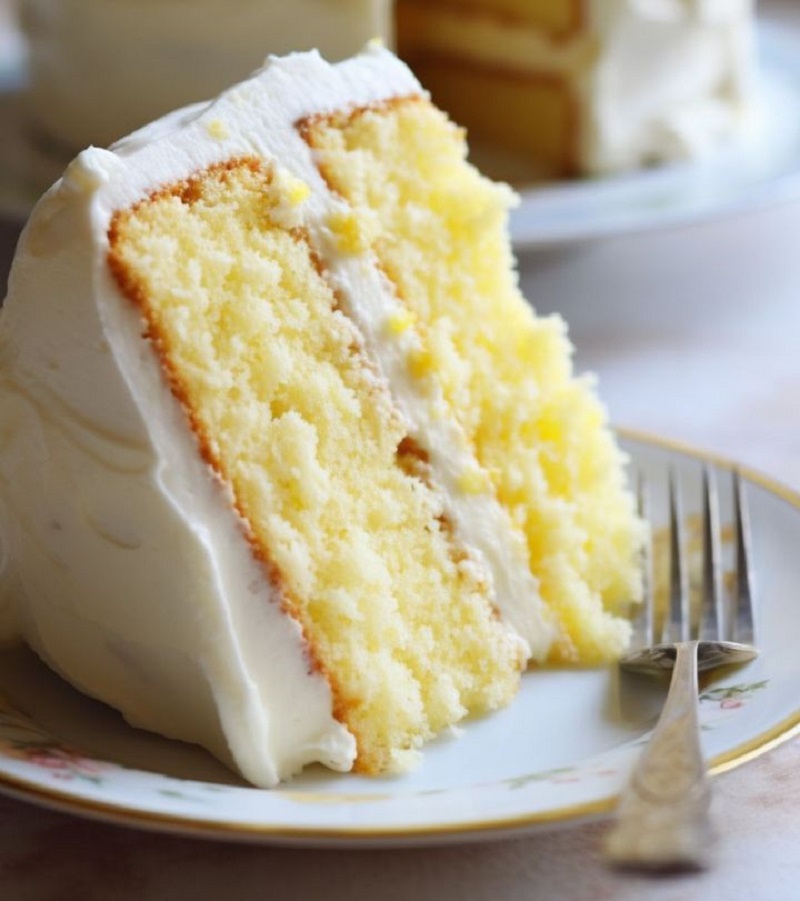 Slice of three-layer lemon cake with white frosting on plate with fork