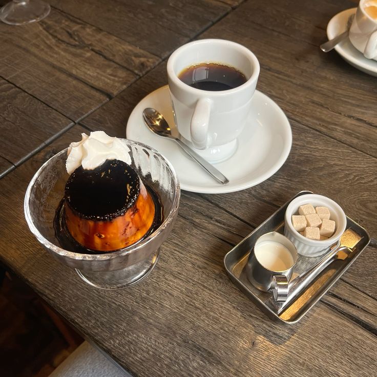 Caramel pudding with whipped cream next to a cup of black coffee on a wooden table